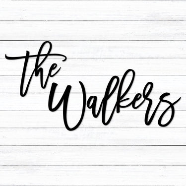 Custom black powder coated last name the Walkers metal sign in an elegant and fun handwritten script font placed on a white washed shiplap wall. The personalized sign is in two different pieces: the and Walkers.